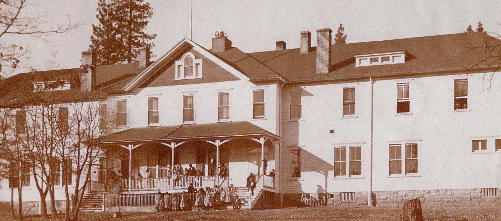 Sepia-toned photograph of a large building with a group standing out front of it